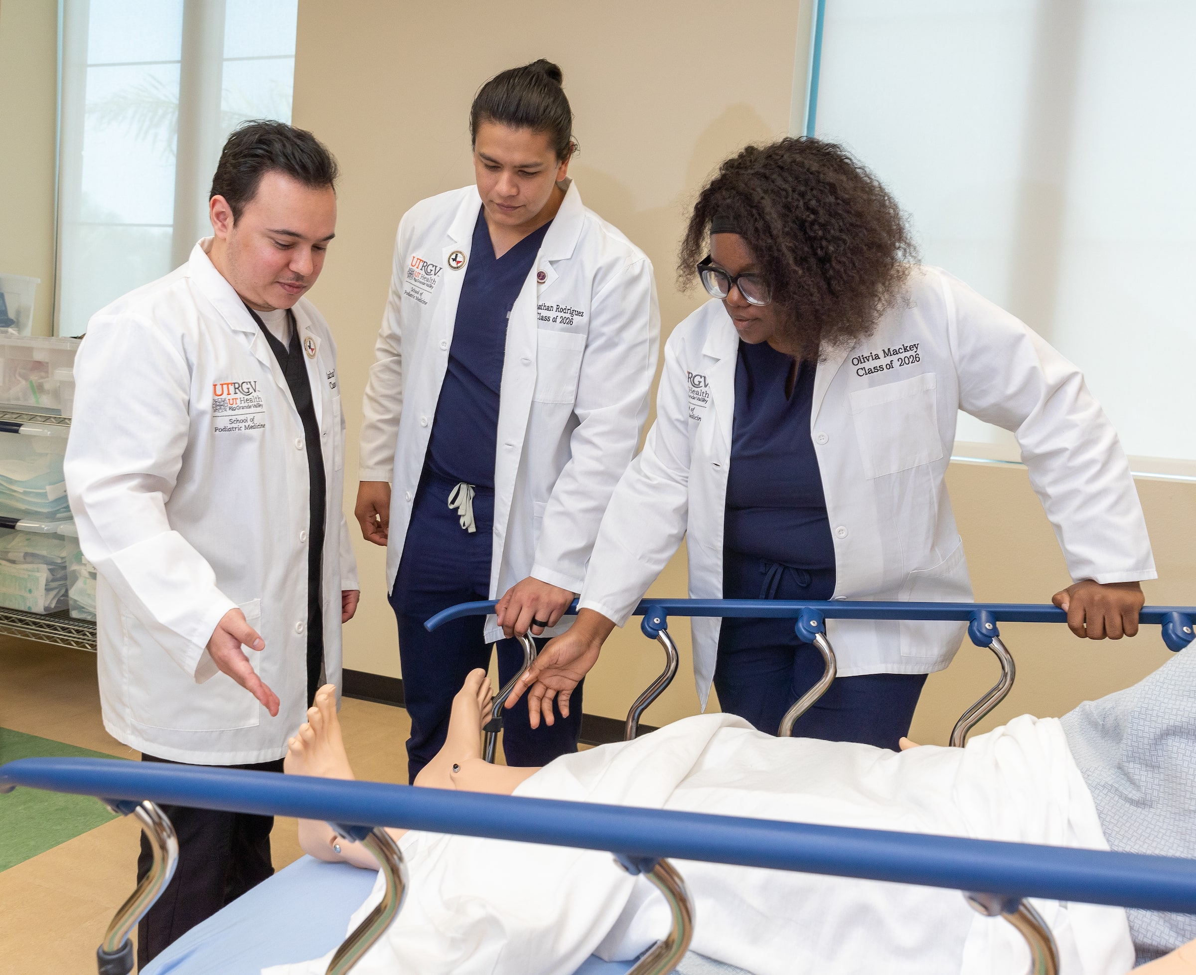 SOPM students assisting patient in a hospital bed.
